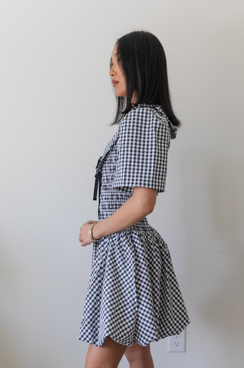 Woman wearing a black and white checkered gingham mini dress with oversized collar against a plain background