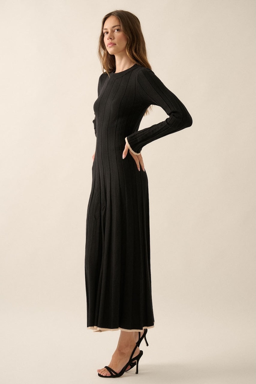 Woman wearing a black knit sweater dress with long sleeves, round neckline and contrast trim in beige.