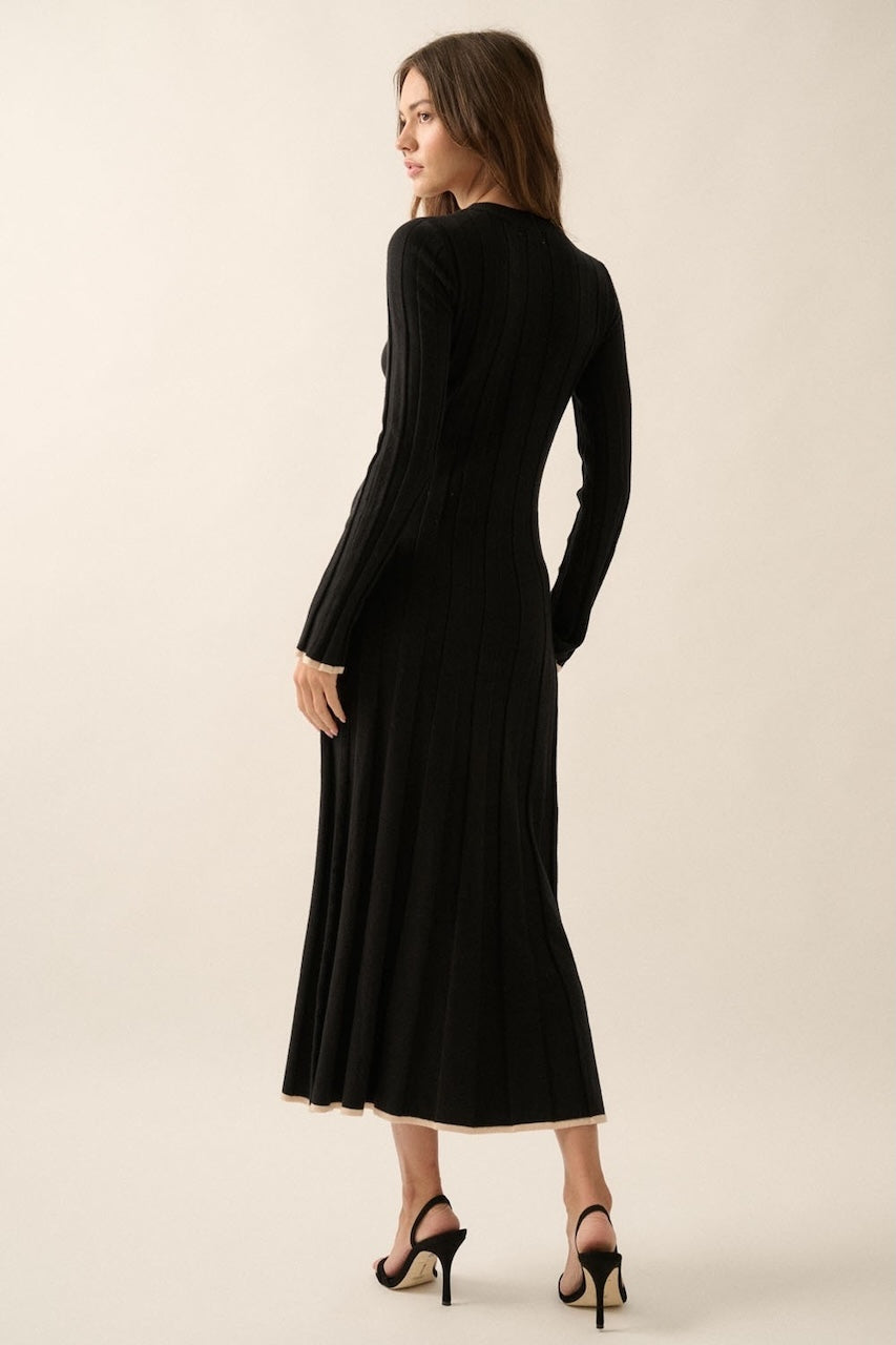 Woman wearing a black knit sweater dress with long sleeves, round neckline and contrast trim in beige.