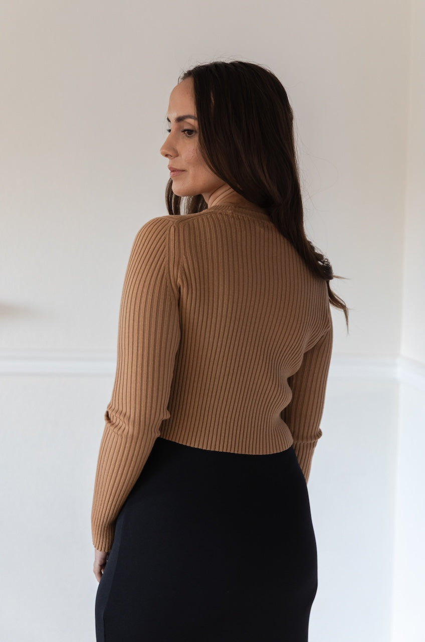 Woman wearing a fitted brown long sleeve crop top with ribbed texture and crew neckline, styled with a black fitted high waisted midi skirt.