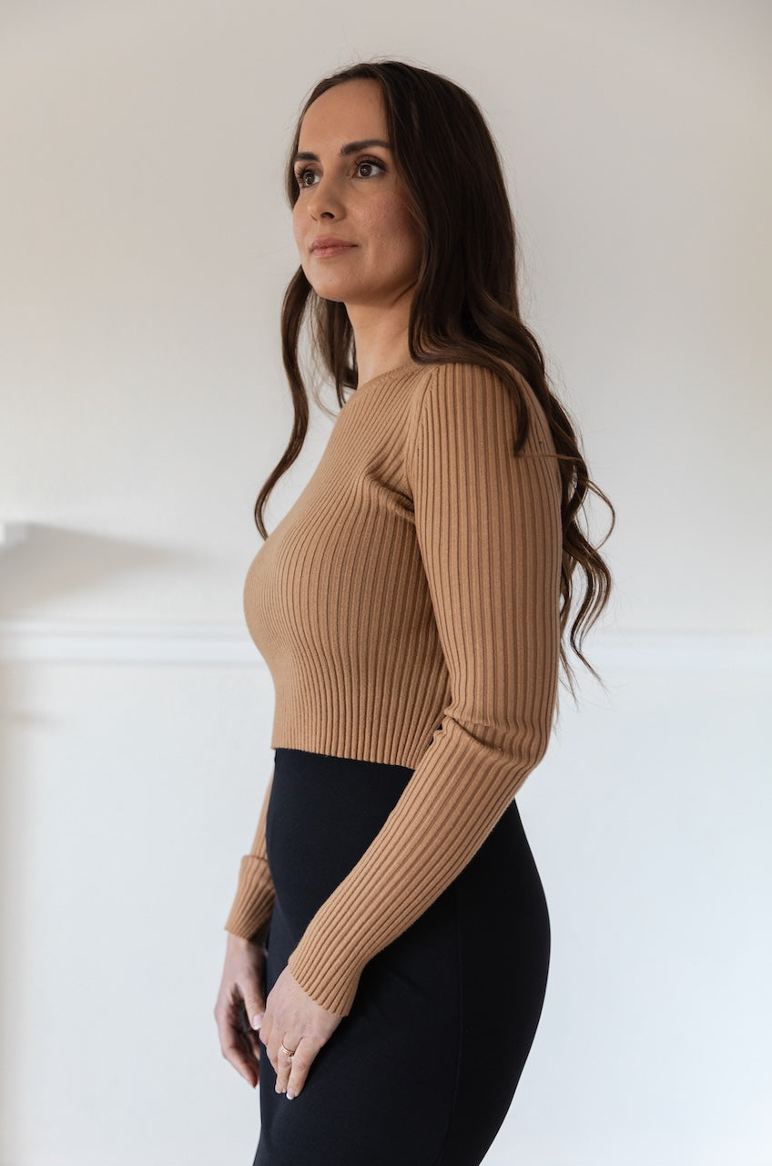 Woman wearing a fitted brown long sleeve crop top with ribbed texture and crew neckline, styled with a black fitted high waisted midi skirt.