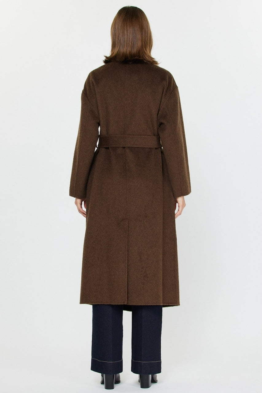 Woman wearing long brown wool coat with oversized fit and belted waist styled over jeans and boots.