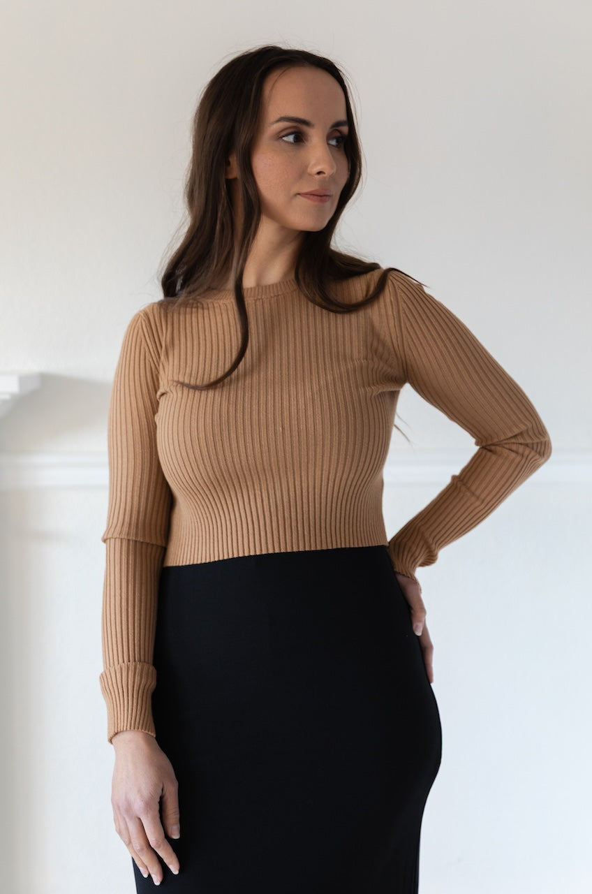 Woman wearing a fitted brown long sleeve crop top with ribbed texture and crew neckline, styled with a black fitted high waisted midi skirt.