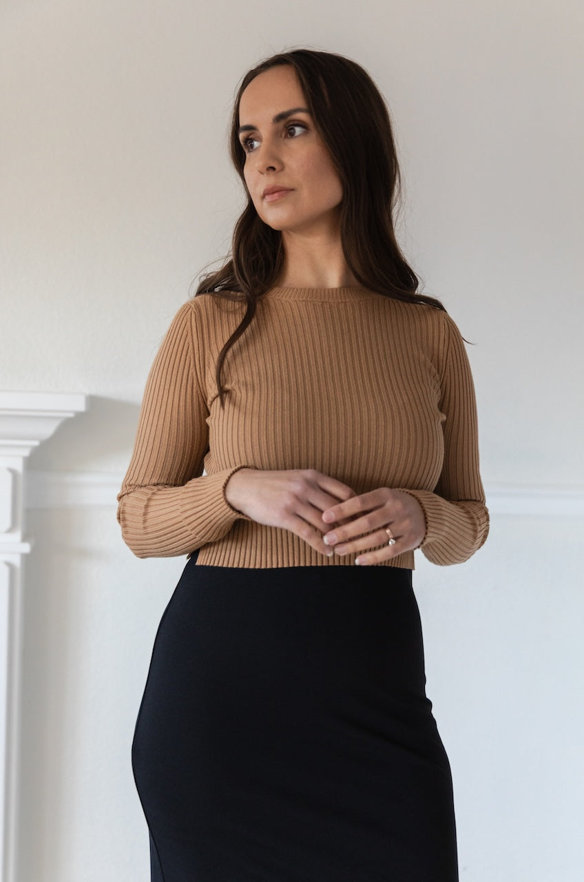 Woman wearing a fitted brown long sleeve crop top with ribbed texture and crew neckline, styled with a black fitted high waisted midi skirt.