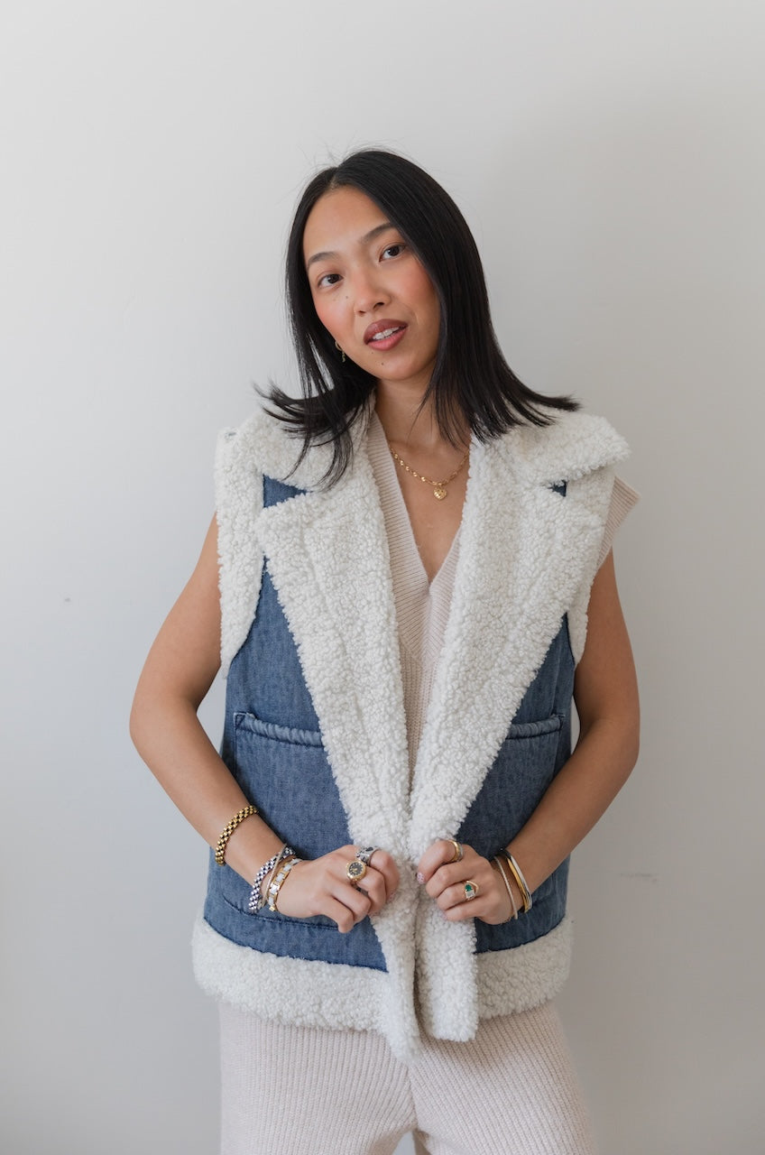Woman wearing a blue denim vest with white fur trim against a plain background
