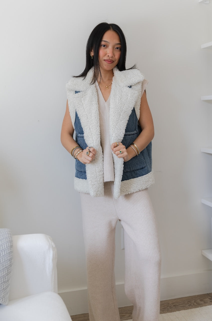 Woman wearing a denim vest with white fur lining in a minimal indoor setting.