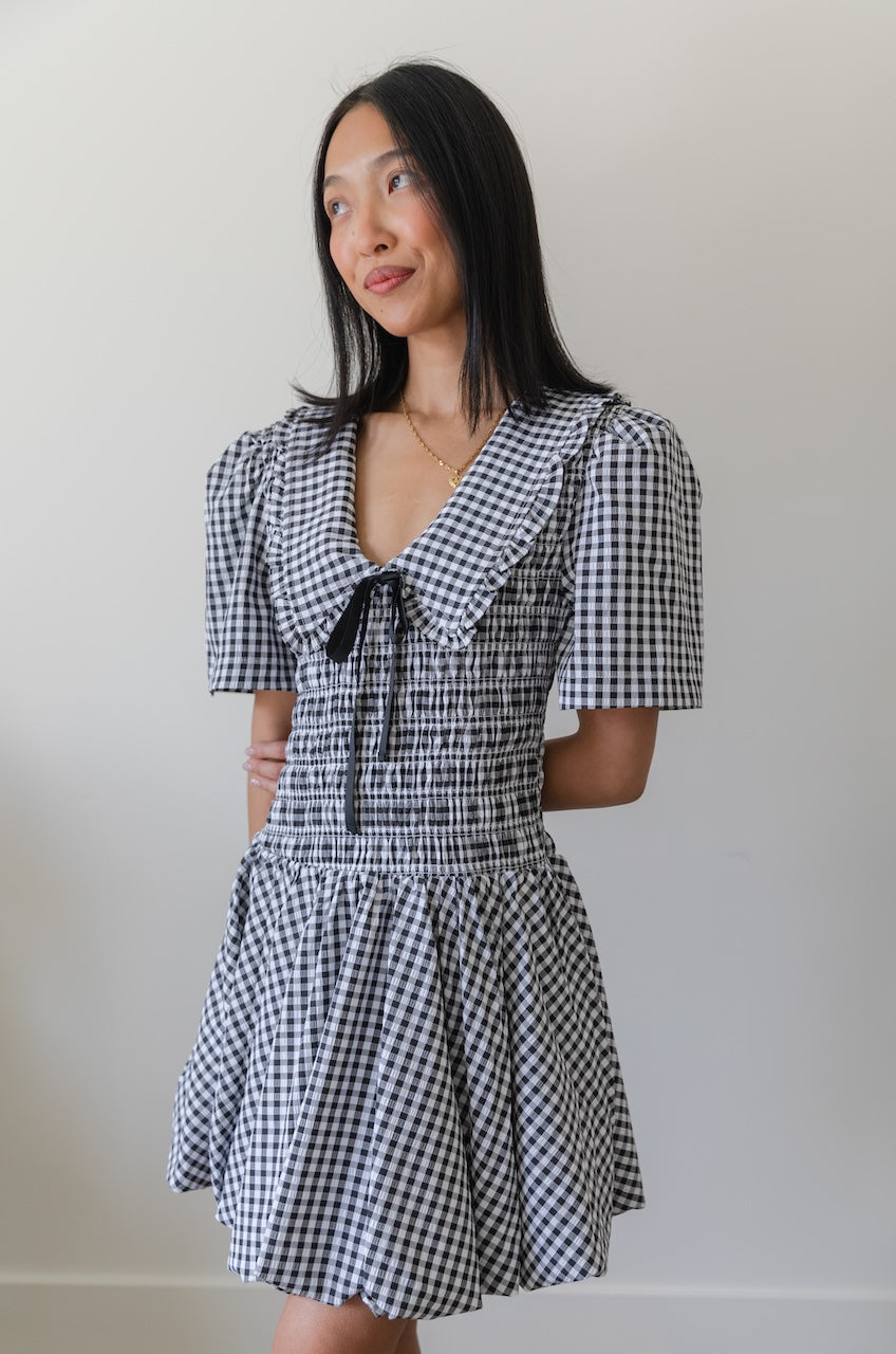 Woman wearing a black and white checkered gingham mini dress with oversized collar against a plain background