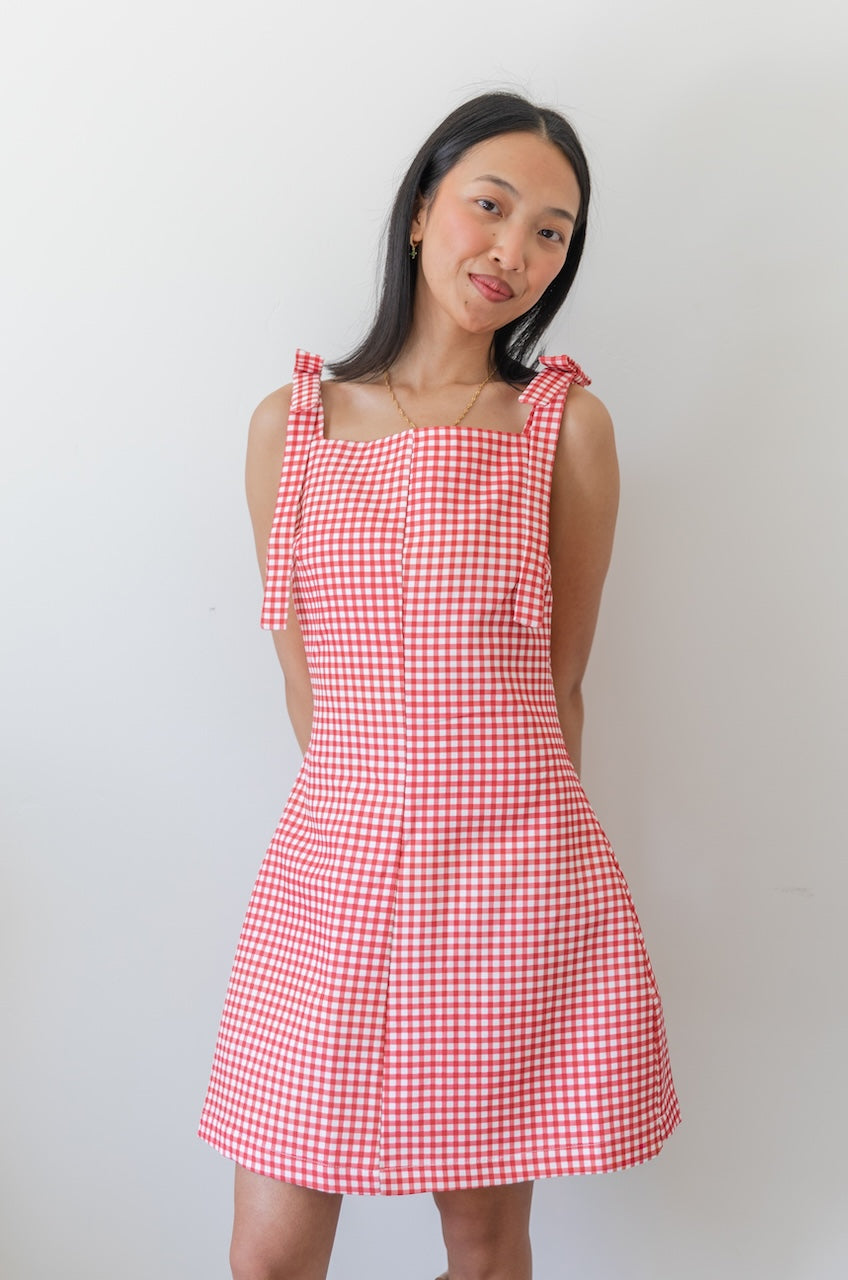Woman wearing a red and white checkered gingham dress with floral boots on a plain background