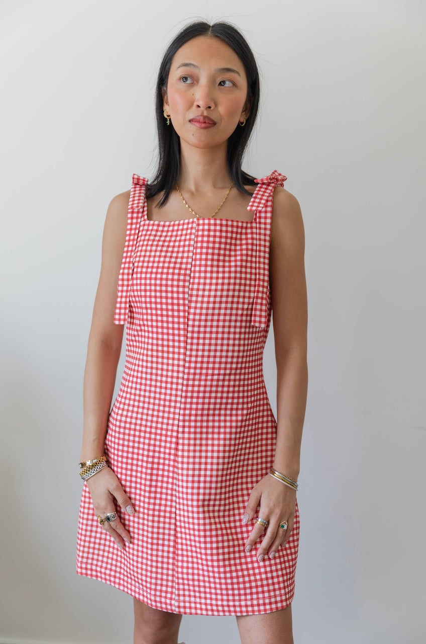Woman wearing a red and white checkered gingham dress with floral boots on a plain background