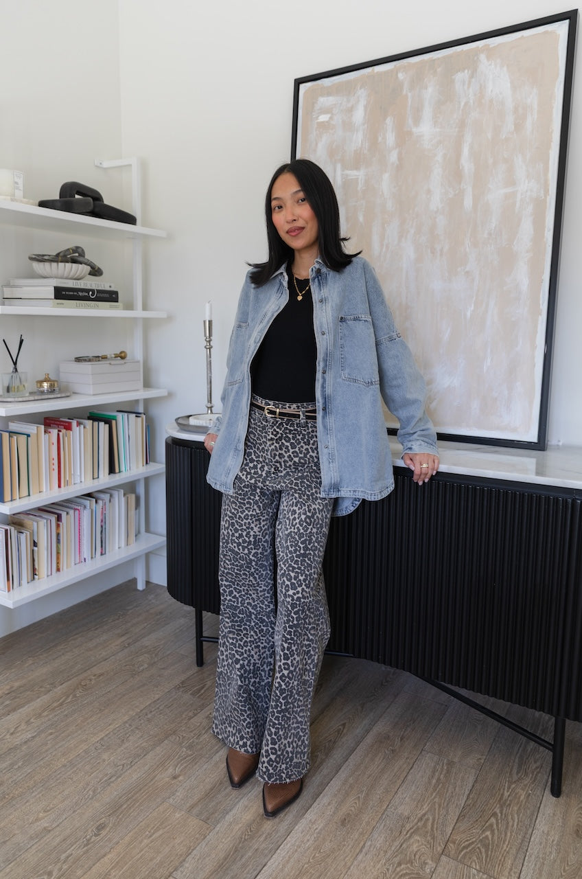 Woman wearing a denim trucker jacket and leopard print pants in an indoor setting