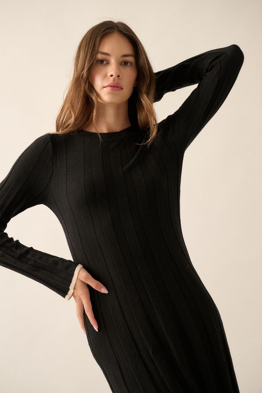 Woman wearing a black knit sweater dress with long sleeves, round neckline and contrast trim in beige.