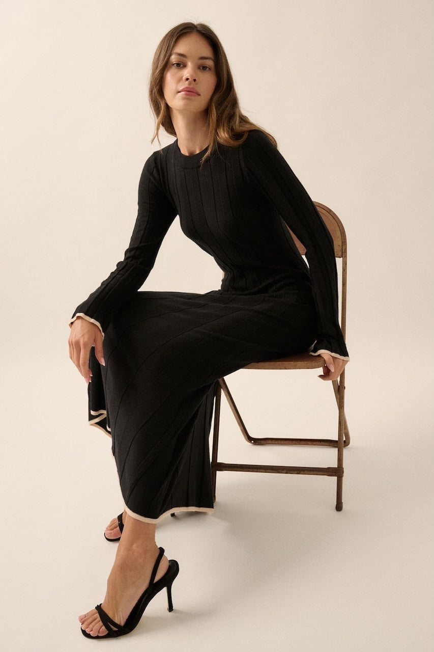 Woman wearing a black knit sweater dress with long sleeves, round neckline and contrast trim in beige.