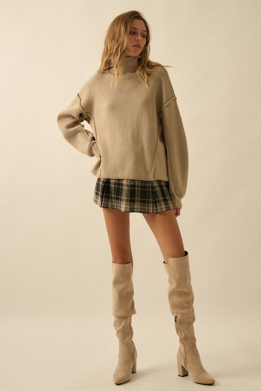 Fall outfit of a woman wearing a plaid mini skirt and beige knee-high boots with a beige oversized sweater