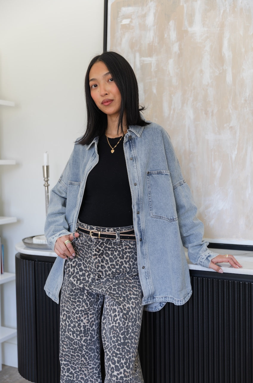 Woman wearing a denim trucker jacket and leopard print pants in an indoor setting