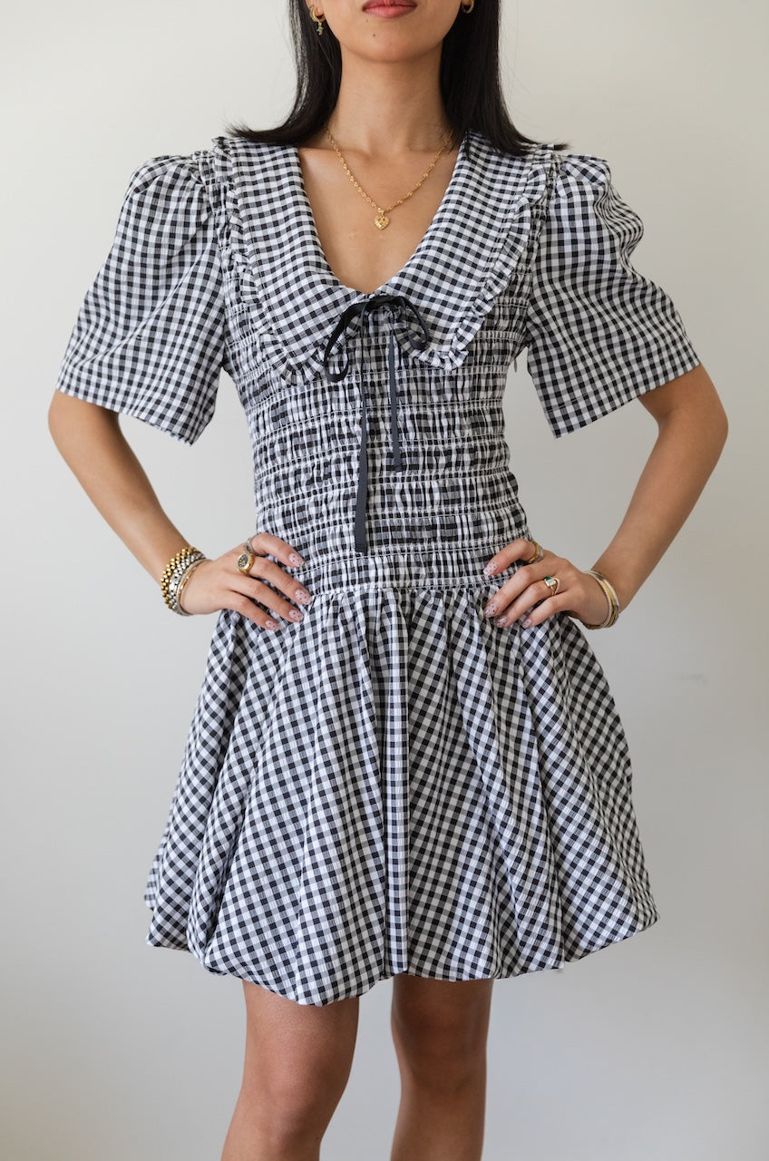 Woman wearing a black and white checkered gingham mini dress with oversized collar against a plain background