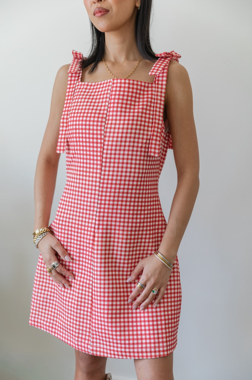 Woman wearing a red and white checkered gingham dress with floral boots on a plain background