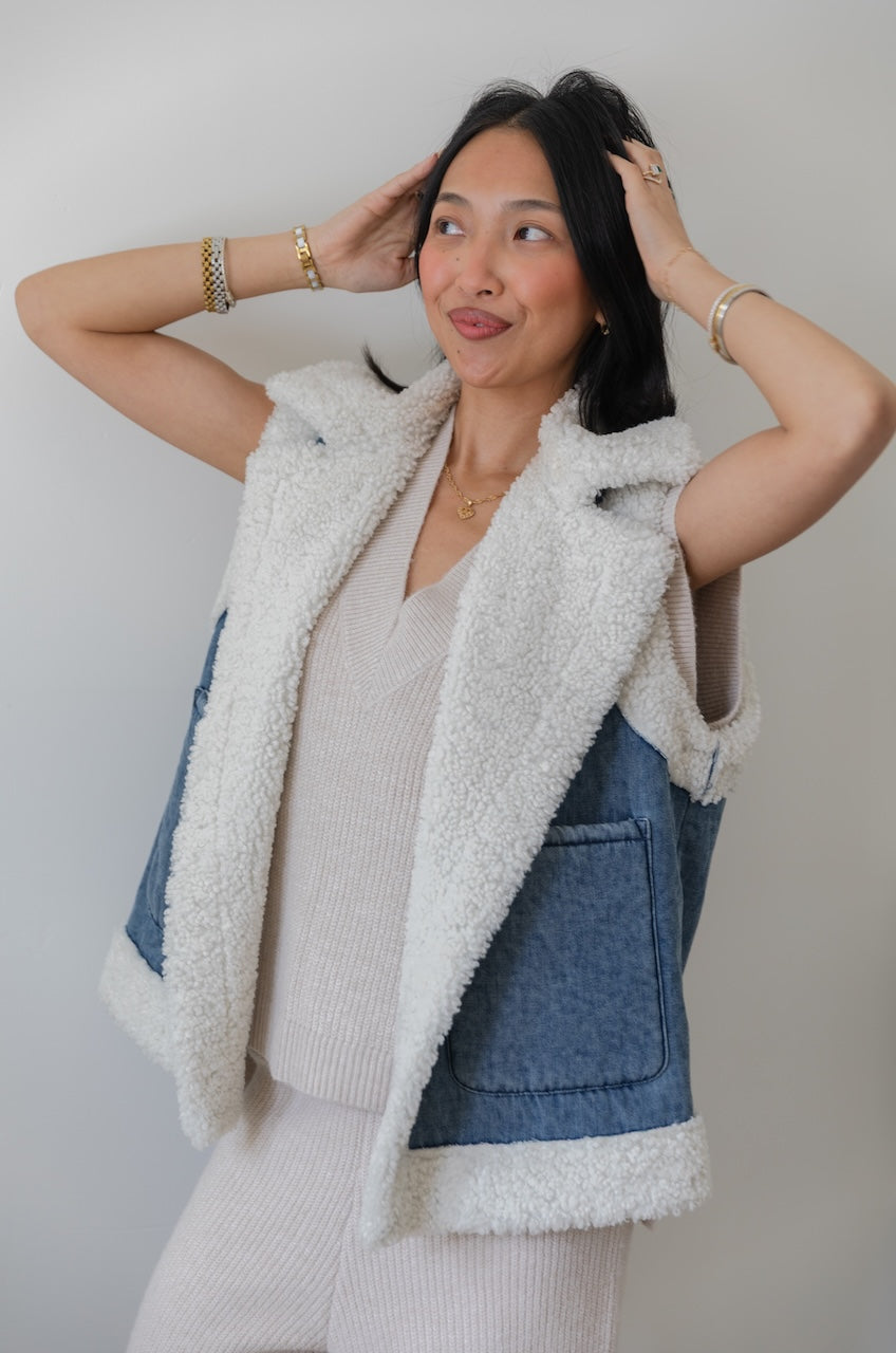 Woman wearing a denim vest with white fleece lining against a plain background