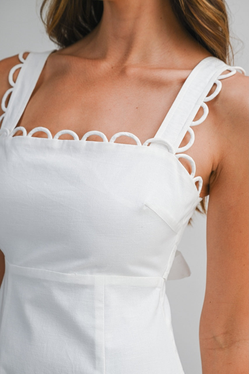 White linen midi dress with square neckline, loop trim straps and scalloped hem on model