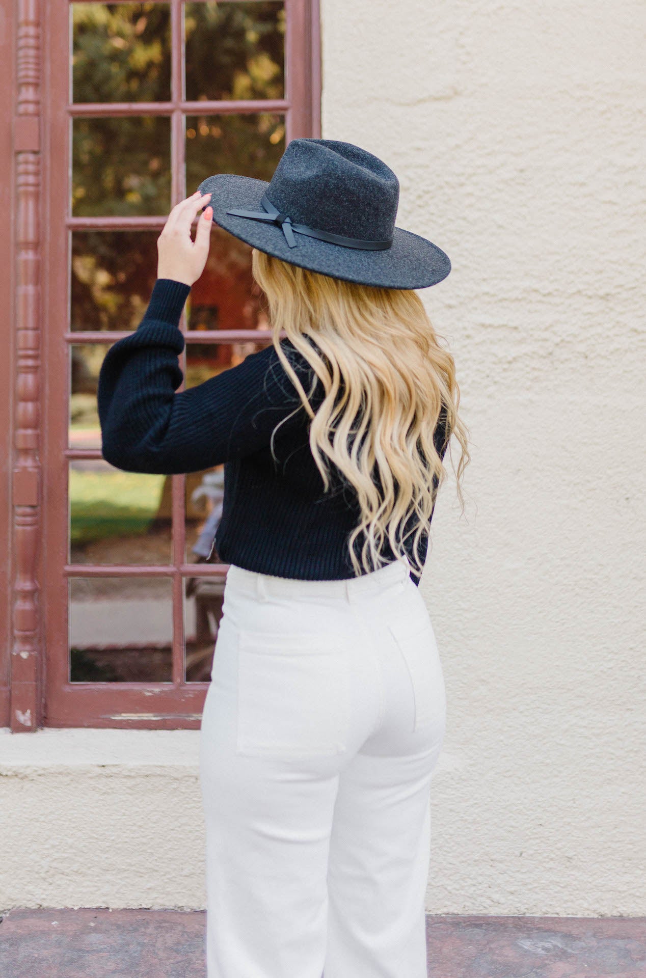 cozy long sleeve black knit sweater paired with high waisted white jeans and a dark gray wool hat