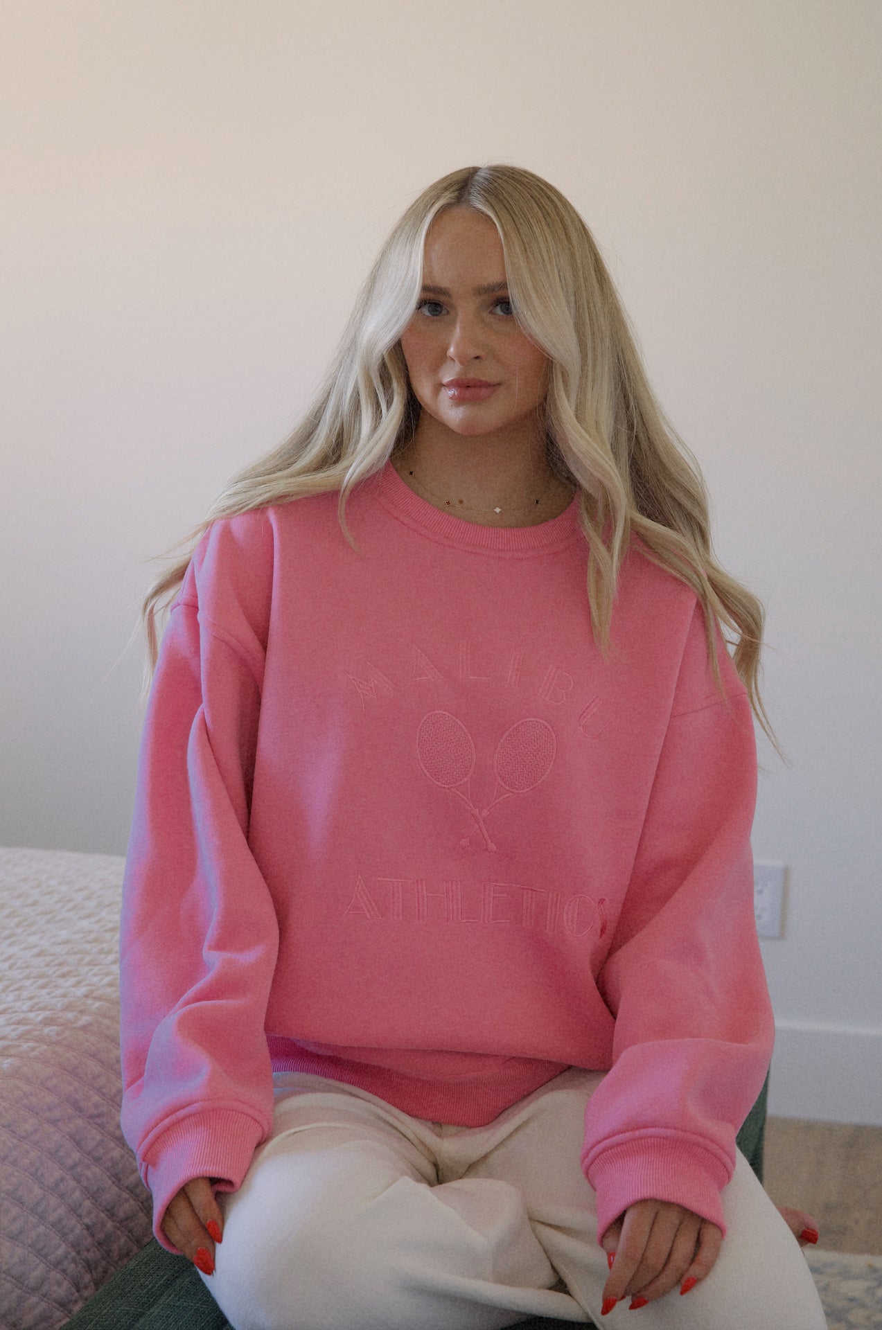 A woman wearing a pink Malibu athletics embroidered graphic sweatshirt crew neck pullover that is a preppy fleece sweatshirt