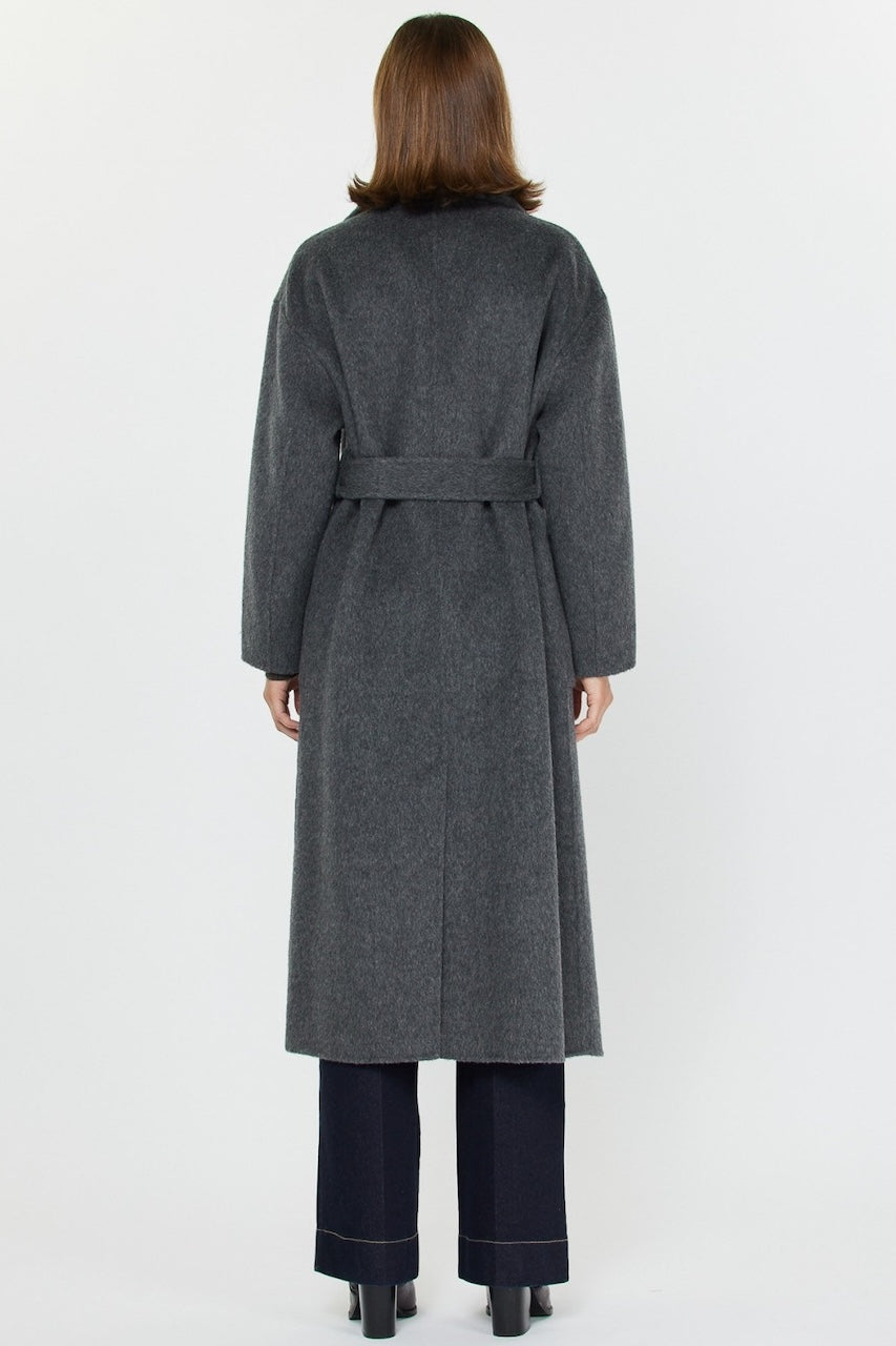 Woman wearing long gray wool coat with oversized fit and belted waist styled over jeans and boots.