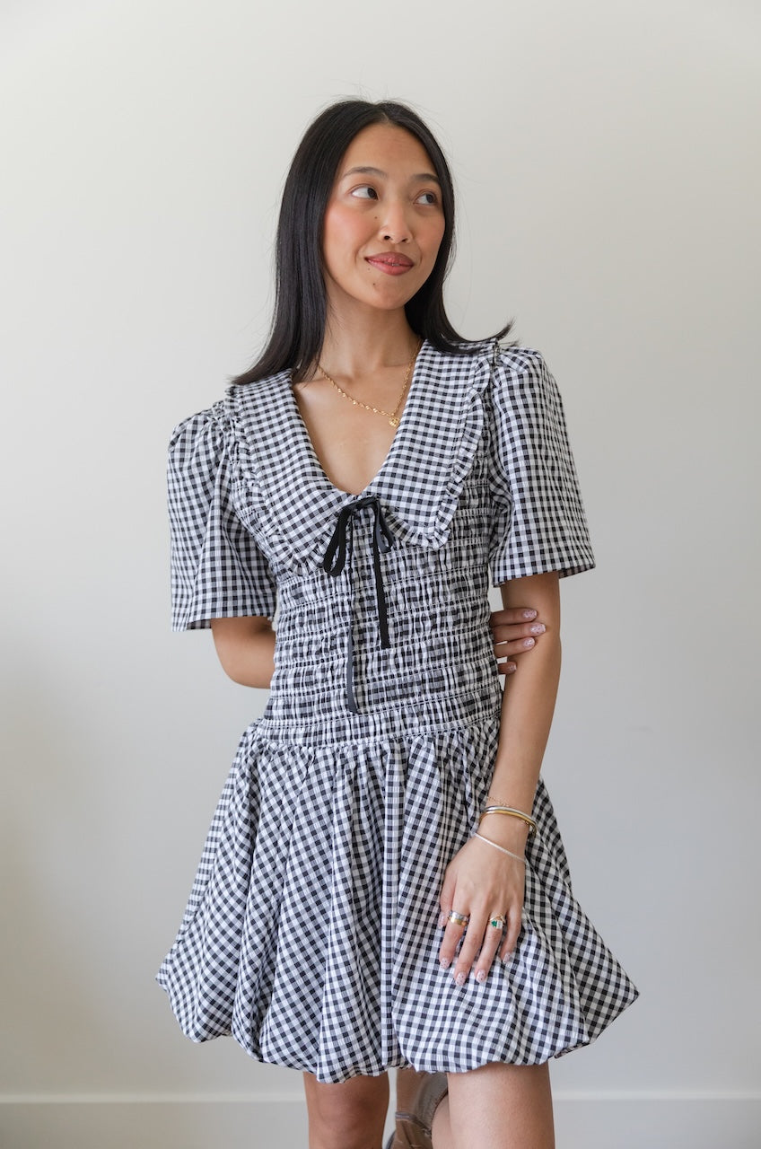Woman wearing a black and white checkered gingham mini dress with oversized collar against a plain background