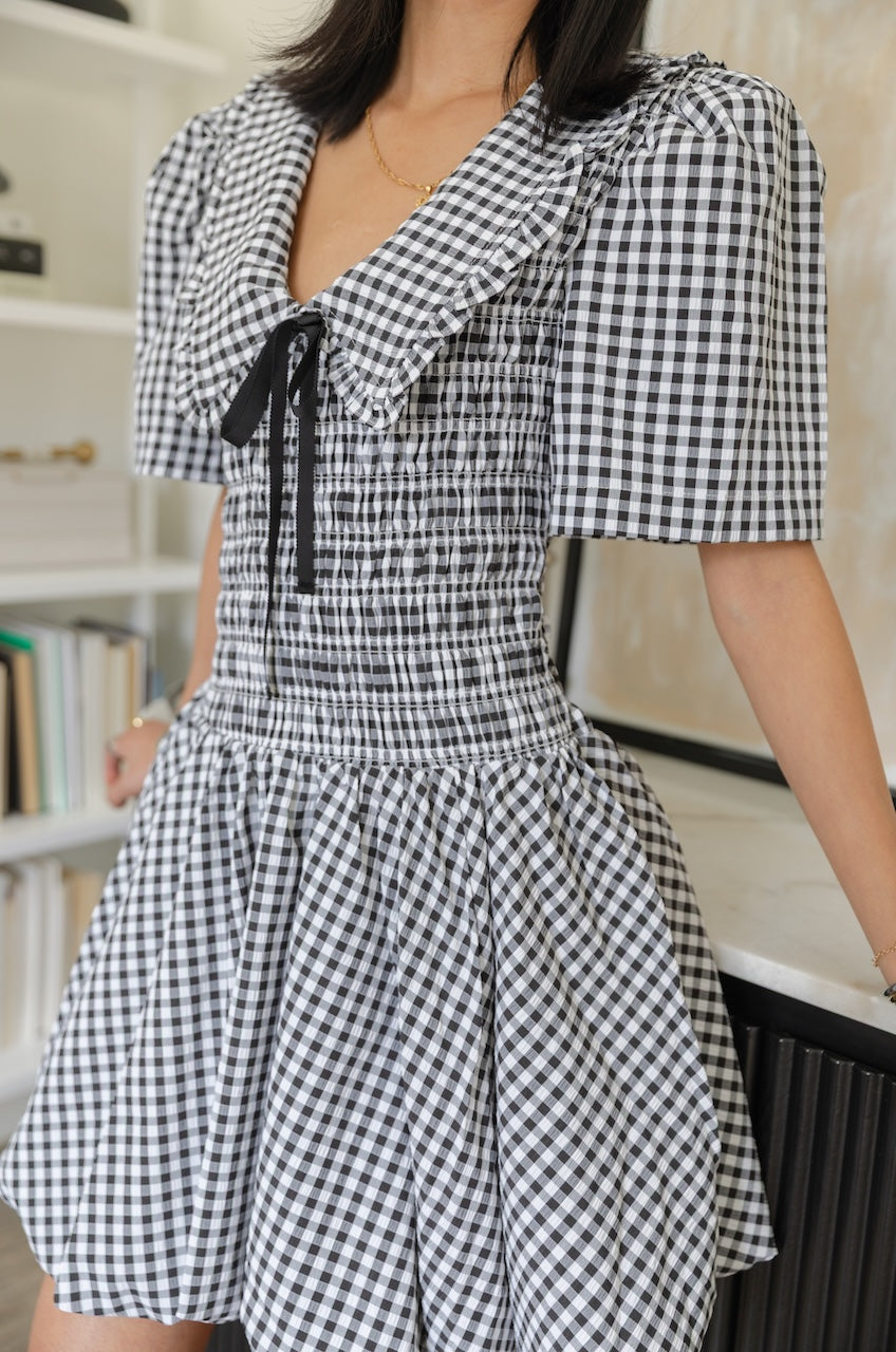 Woman wearing a black and white checkered gingham mini dress with oversized collar against a plain background