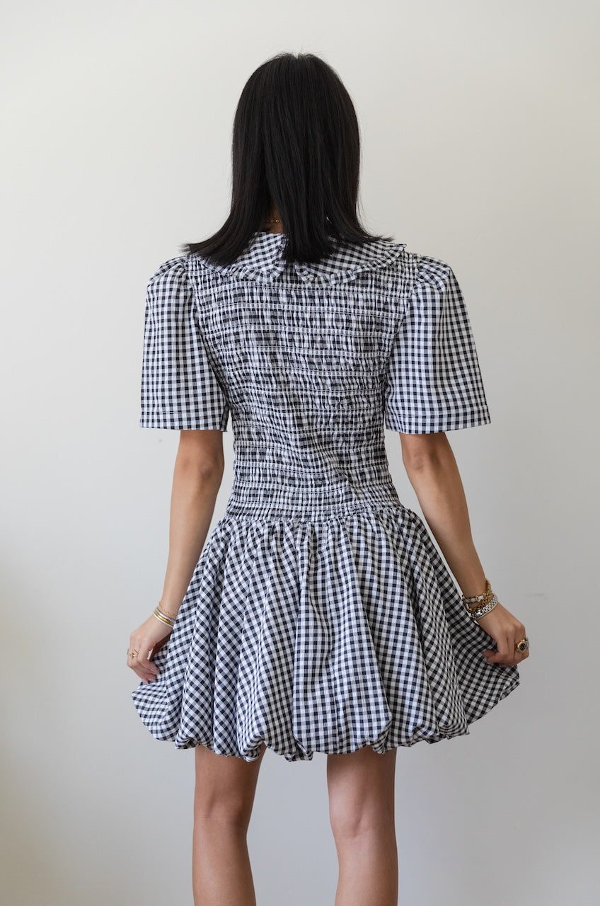 Woman wearing a black and white checkered gingham mini dress with oversized collar against a plain background