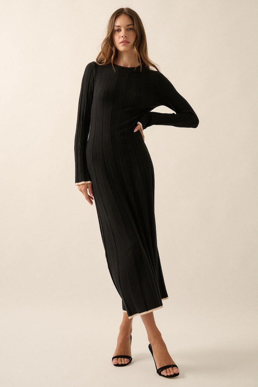 Woman wearing a black knit sweater dress with long sleeves, round neckline and contrast trim in beige.