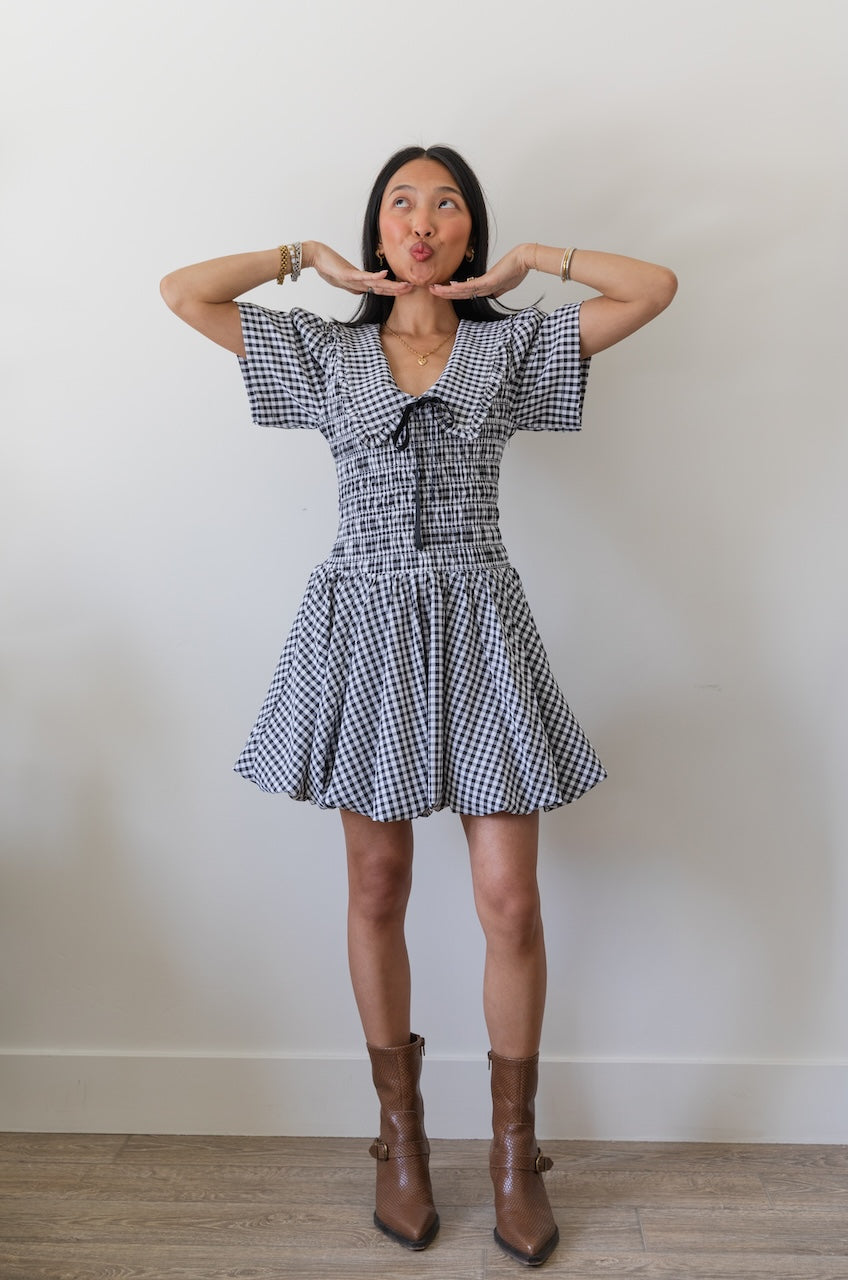 Woman wearing a black and white checkered gingham mini dress with oversized collar against a plain background