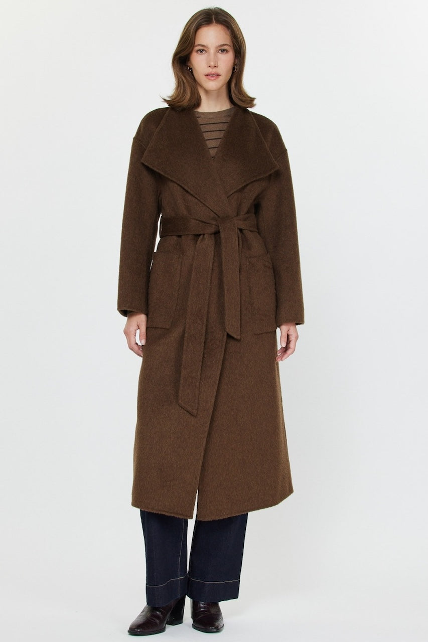 Woman wearing long brown wool coat with oversized fit and belted waist styled over jeans and boots.