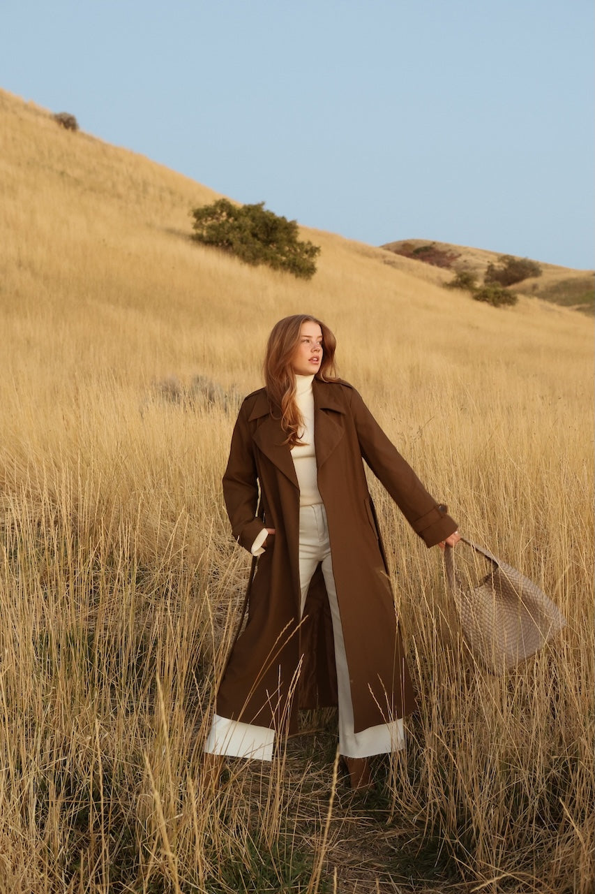 Woman in a brown coat standing in a field with a clear blue sky.