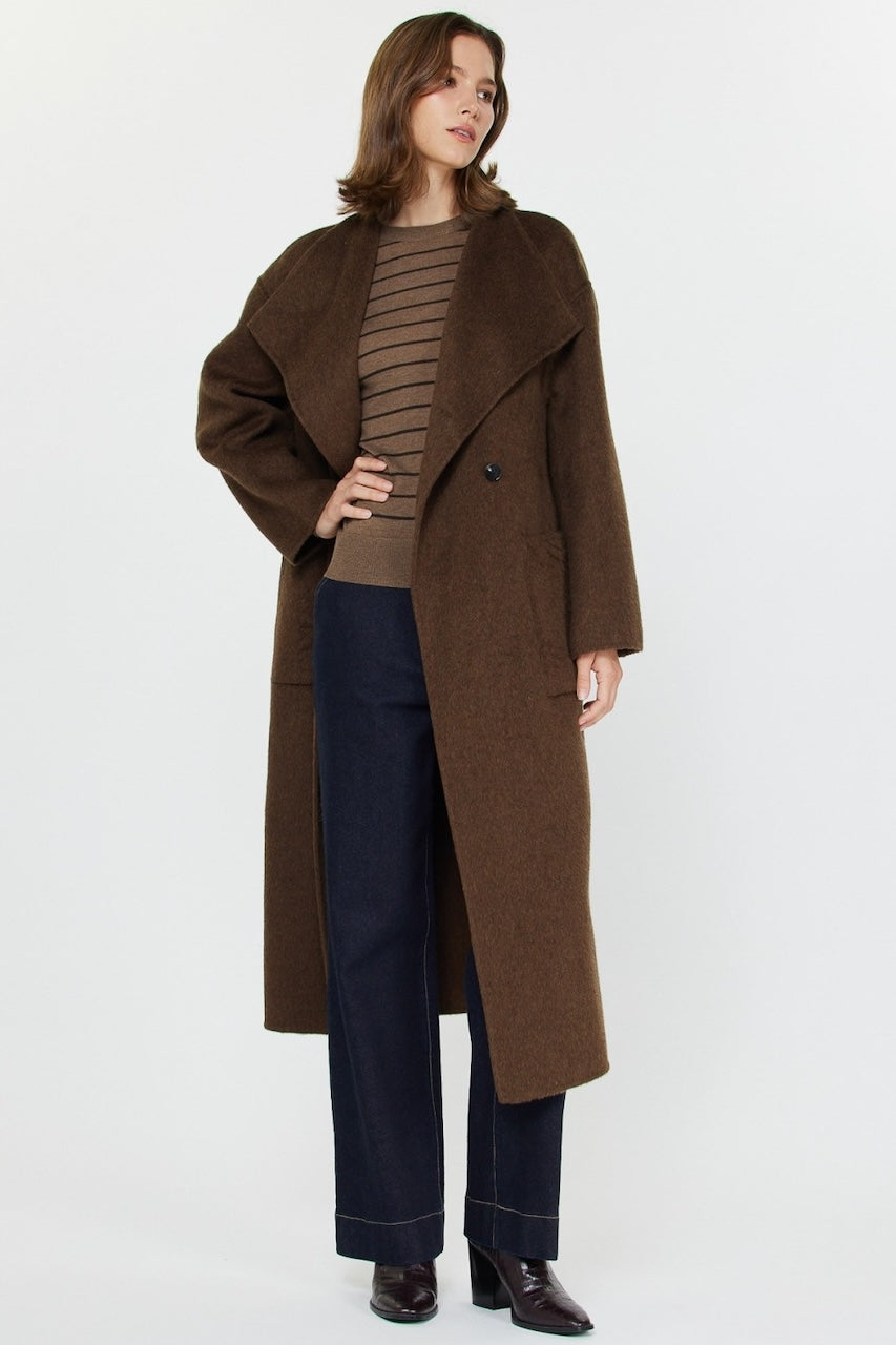 Woman wearing long brown wool coat with oversized fit and belted waist styled over jeans and boots.