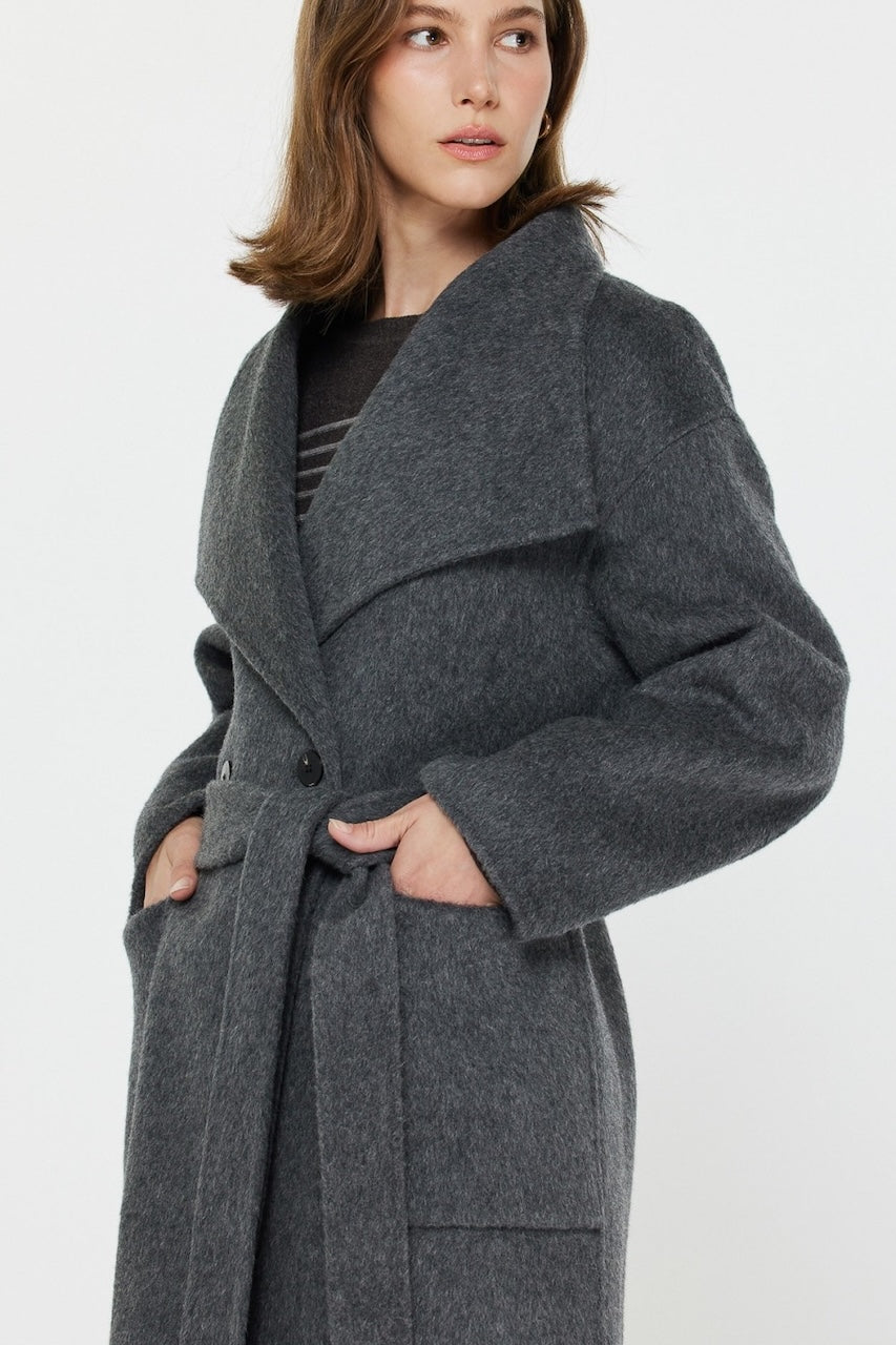 Woman wearing long gray wool coat with oversized fit and belted waist styled over jeans and boots.