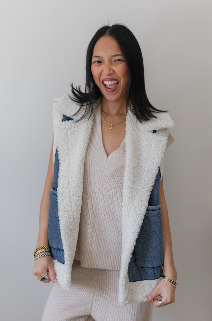 Woman wearing a white fleece vest over a denim jacket with a plain background