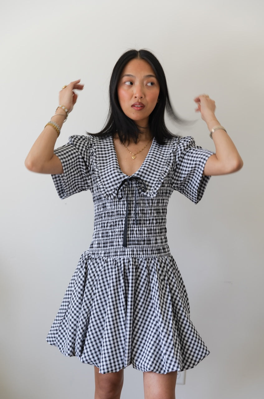 Woman wearing a black and white checkered gingham mini dress with oversized collar against a plain background