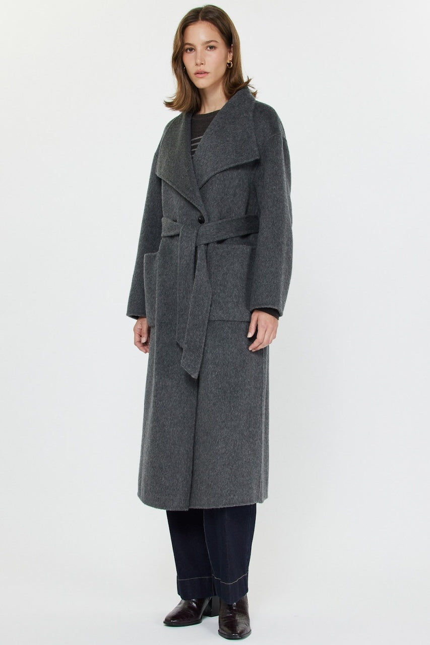 Woman wearing long gray wool coat with oversized fit and belted waist styled over jeans and boots.