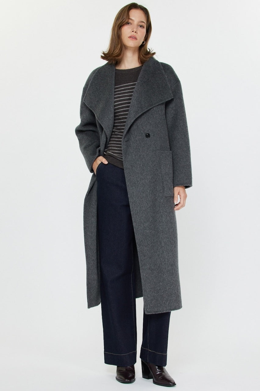 Woman wearing long gray wool coat with oversized fit and belted waist styled over jeans and boots.