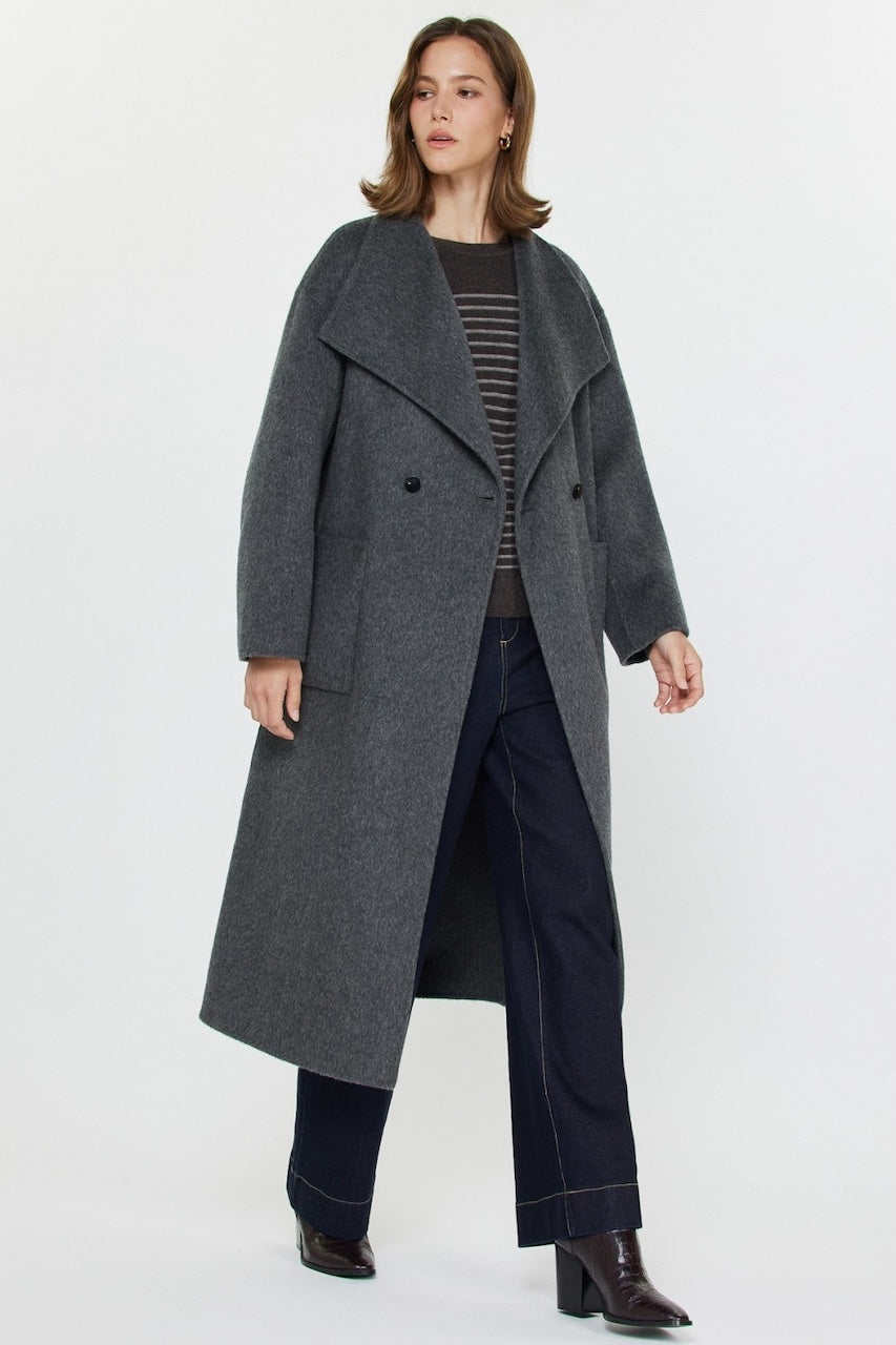 Woman wearing long gray wool coat with oversized fit and belted waist styled over jeans and boots.