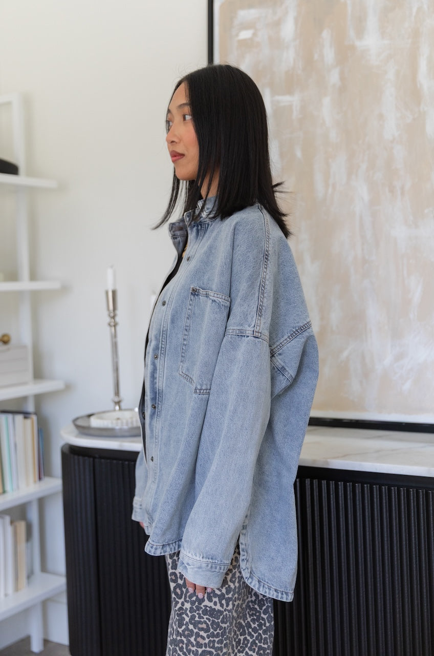 woman wearing a denim jacket in a room with a white wall and bookshelf.