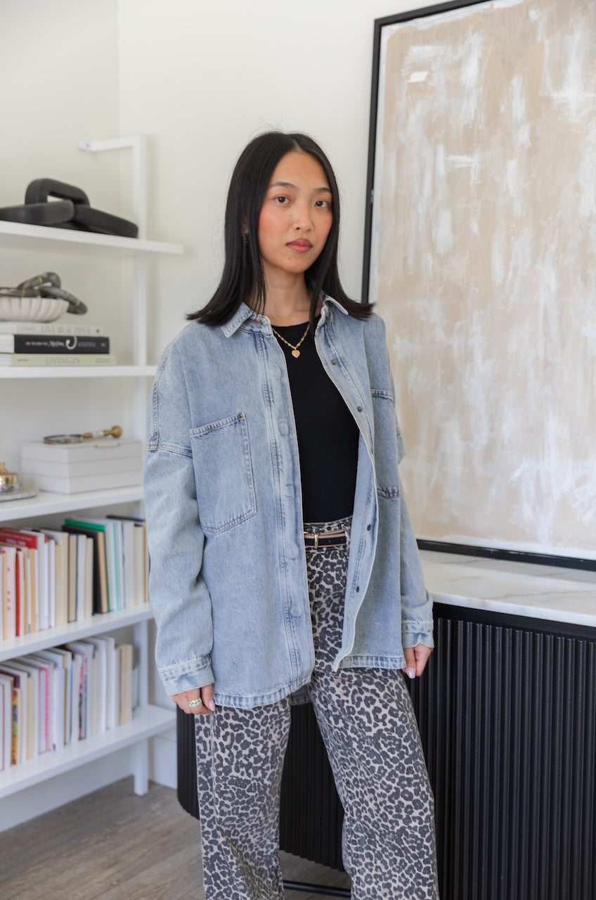 Woman wearing a denim trucker jacket and leopard print pants in an indoor setting