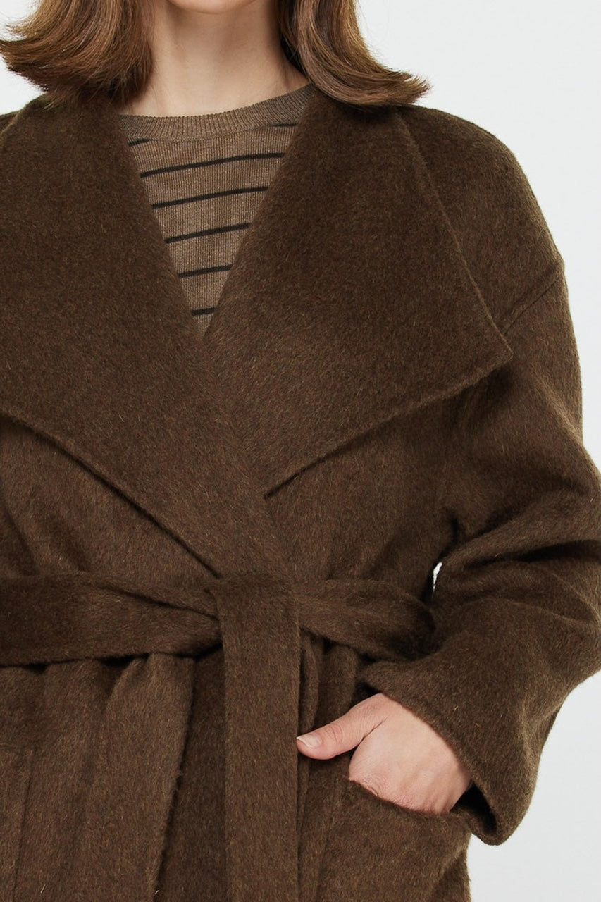 Woman wearing long brown wool coat with oversized fit and belted waist styled over jeans and boots.