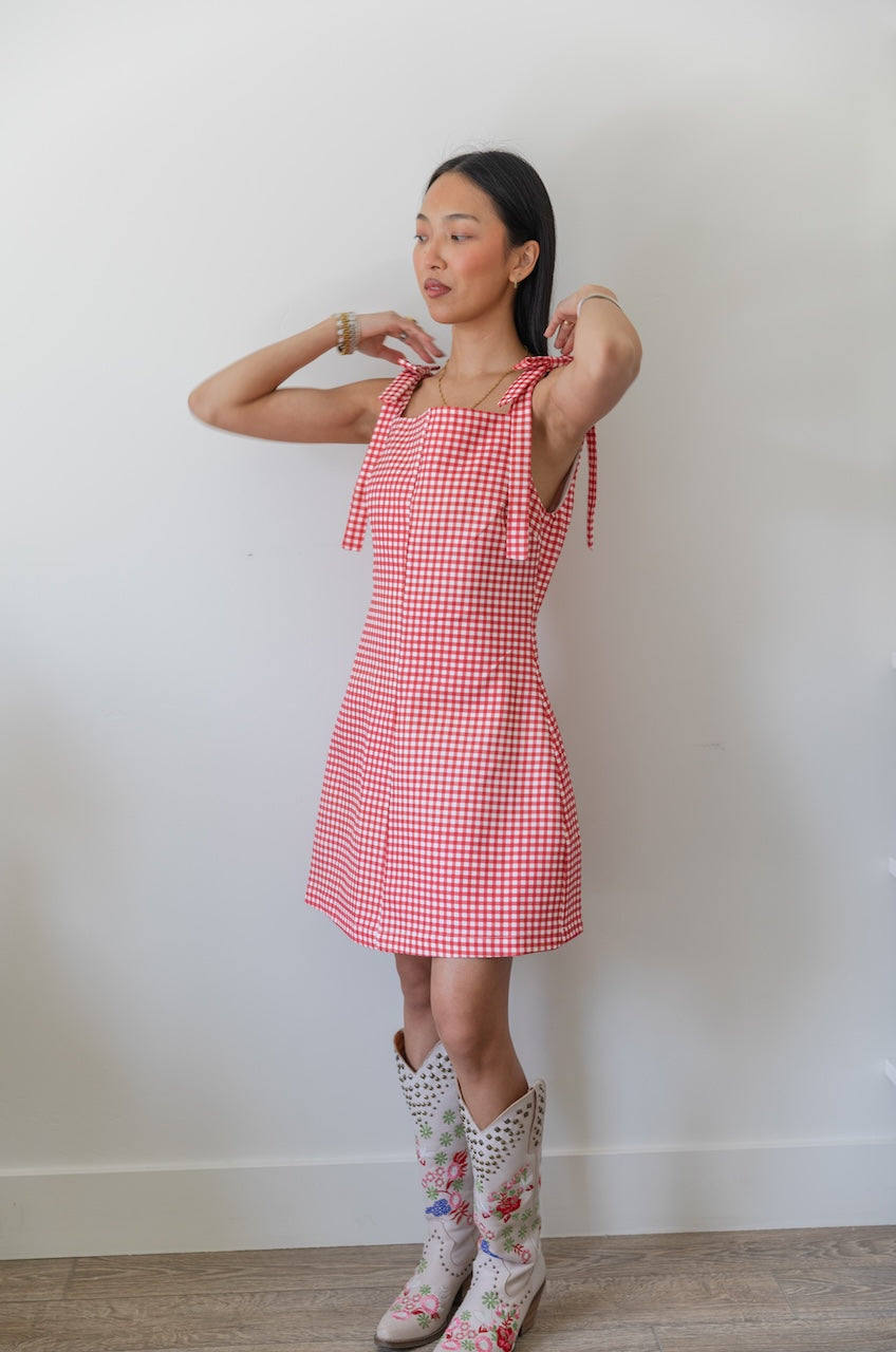 Woman wearing a red and white checkered gingham dress with floral boots on a plain background