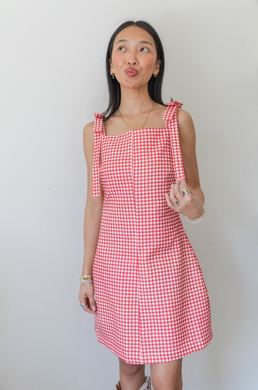 Woman wearing a red and white checkered gingham dress with floral boots on a plain background