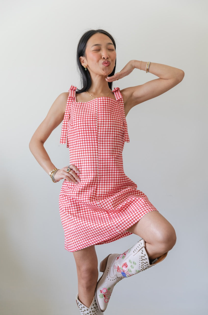 Woman wearing a red and white checkered gingham dress with floral boots on a plain background