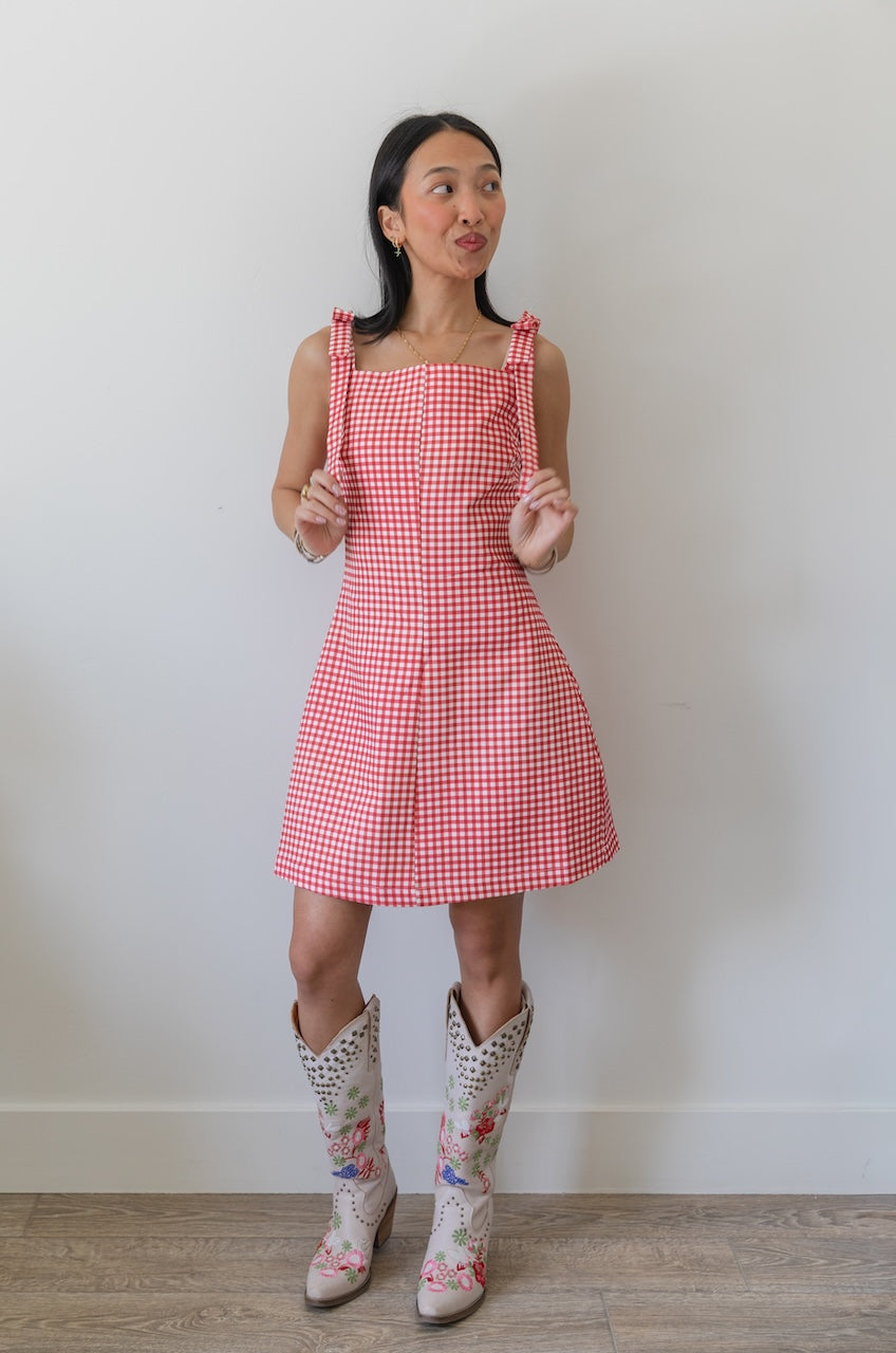Woman wearing a red and white checkered gingham dress with floral boots on a plain background