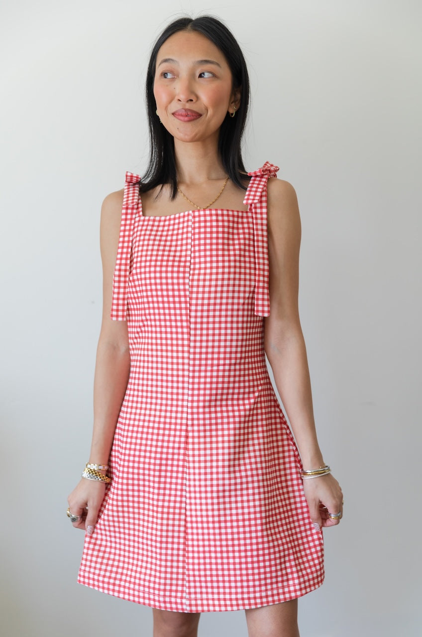 Woman wearing a red and white checkered gingham dress with floral boots on a plain background