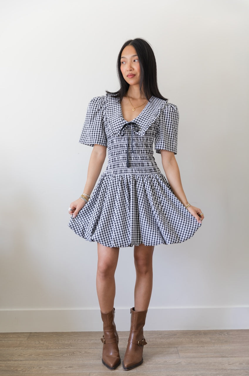 Woman wearing a black and white checkered gingham mini dress with oversized collar against a plain background