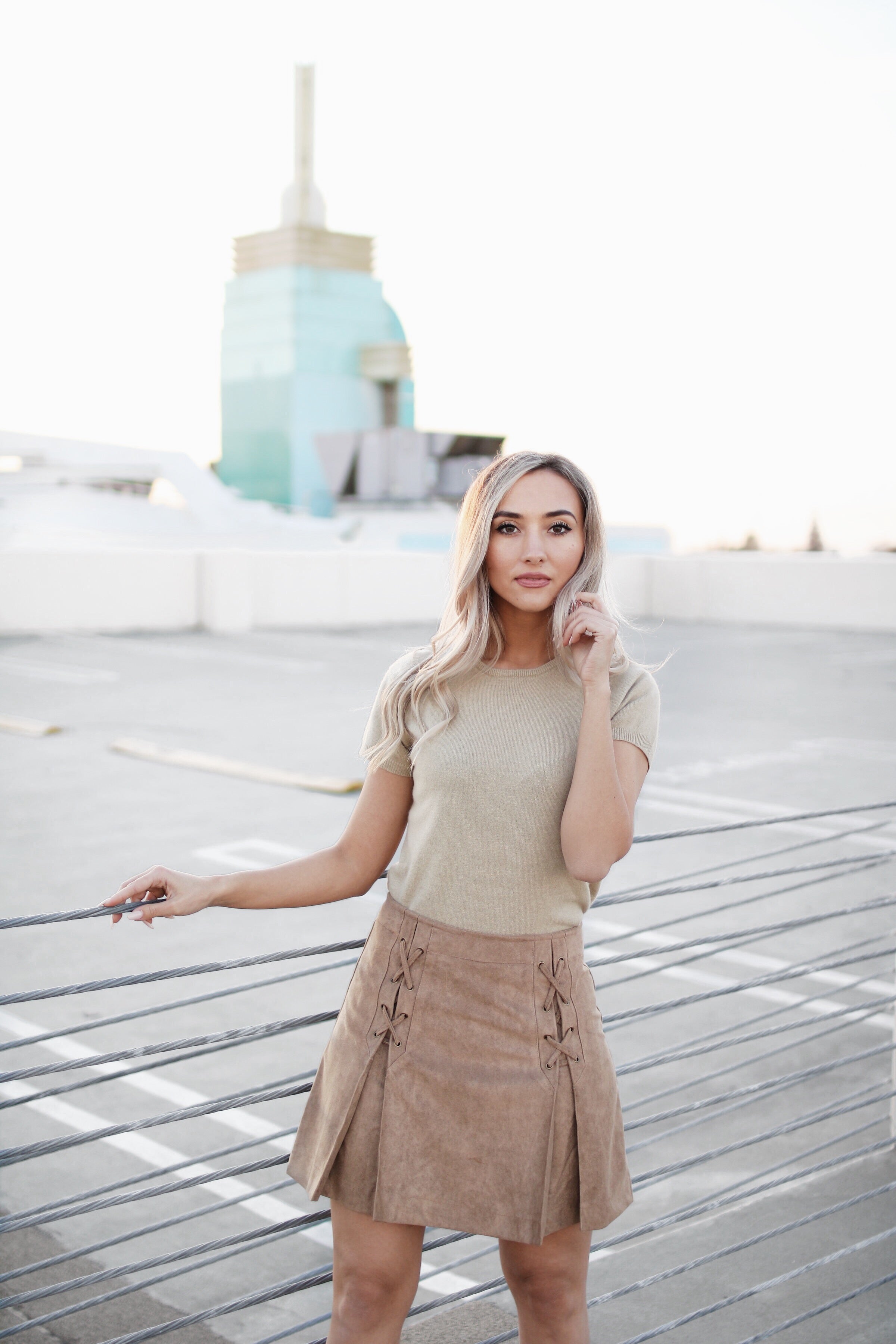 A woman standing on a wooden deck wearing a brown mini skirt with lace up corset detailing and pleats on the front.