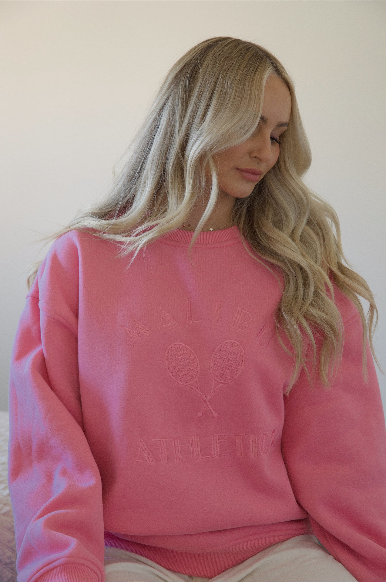A woman wearing a pink Malibu athletics embroidered graphic sweatshirt crew neck pullover that is a preppy fleece sweatshirt